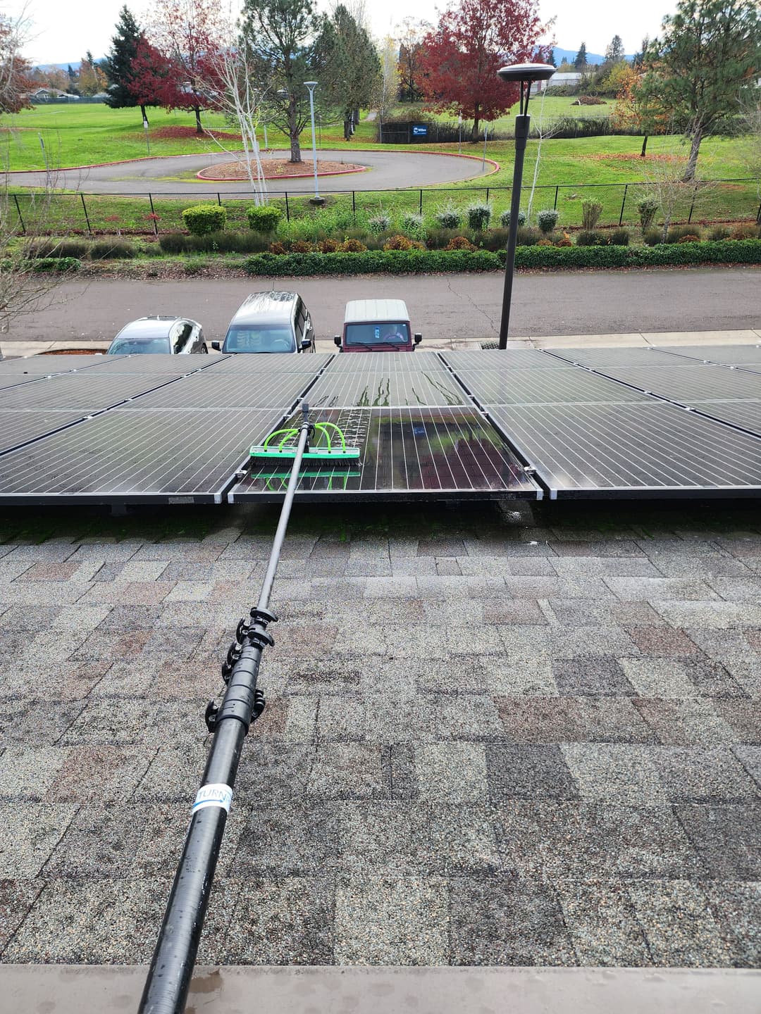 View of solar panels on a roof with cleaning equipment, surrounded by greenery and vehicles.