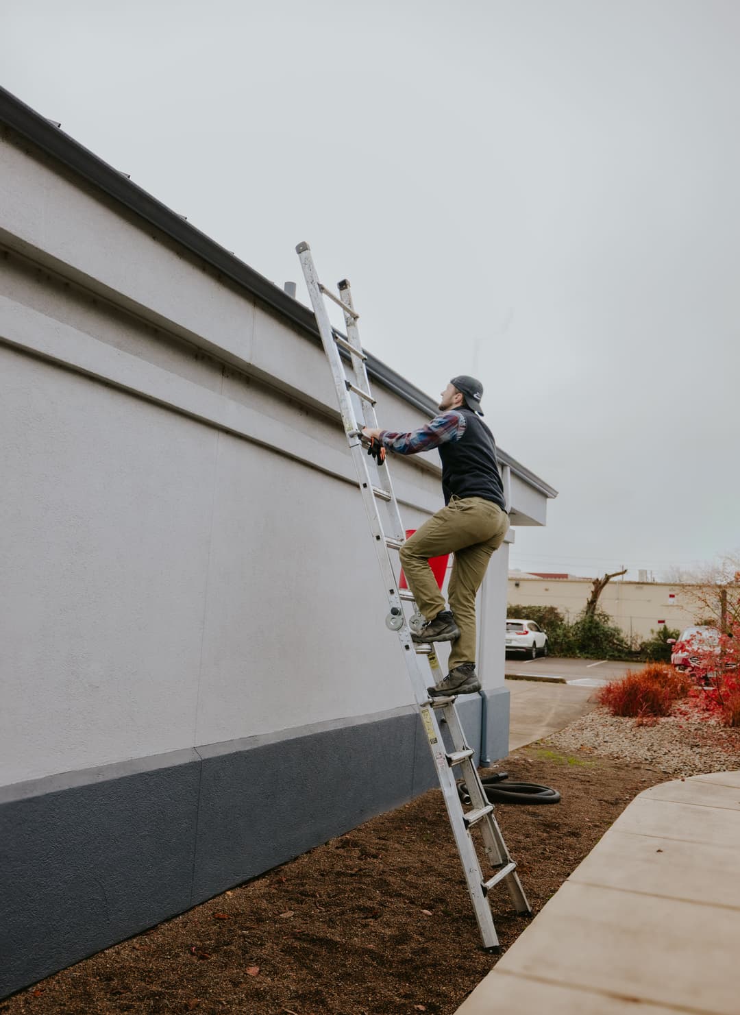 Person climbing a ladder to maintain the exterior of a building on a cloudy day.