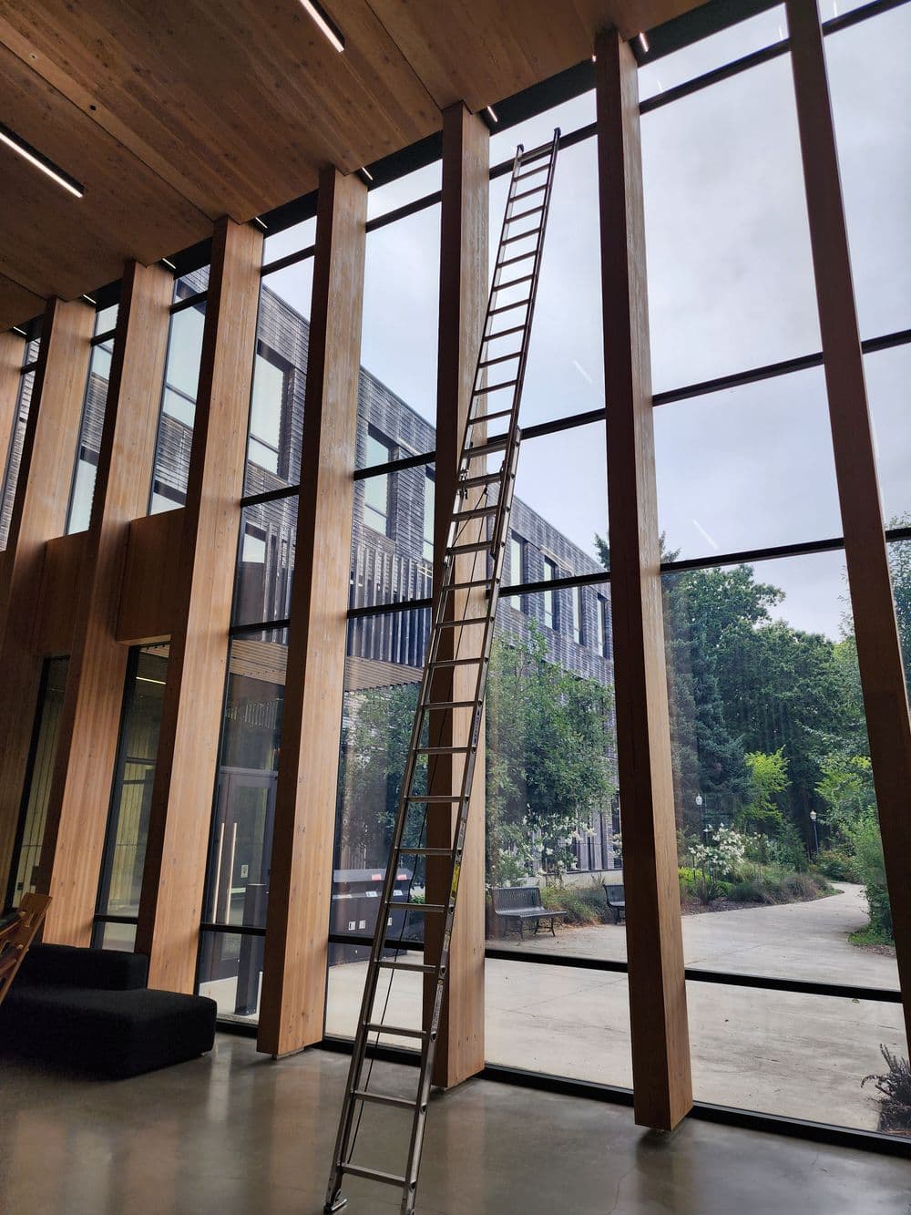 Modern interior with a metal ladder against large glass windows and wooden beams.