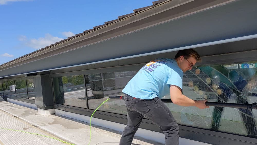 Worker cleaning windows on a modern building under a clear blue sky.